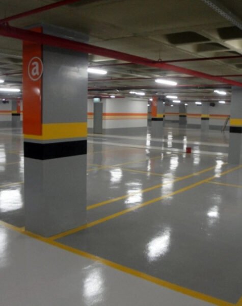 Garagem subterrânea com piso revestido em tinta epóxi cinza — vagas demarcadas, iluminação refletida no acabamento brilhante