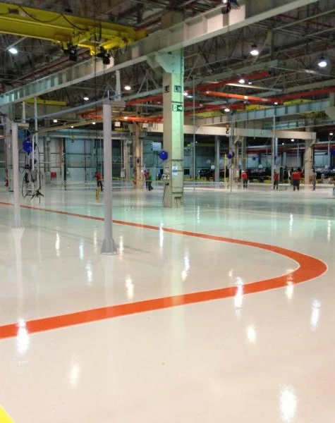 Profissional aplicando tinta epóxi cinza com rolo em piso de concreto de galpão industrial — superfície lisa e uniforme